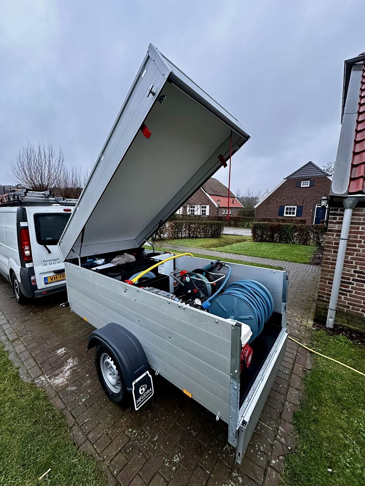 Aanhanger met geopende klep, met daarin de reinigingsinstallatie en een haspel met slang